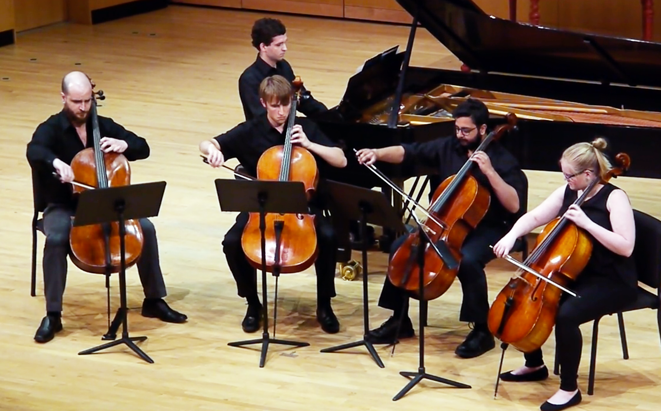 Five musicians — one pianist and four cellists — perform on stage.
