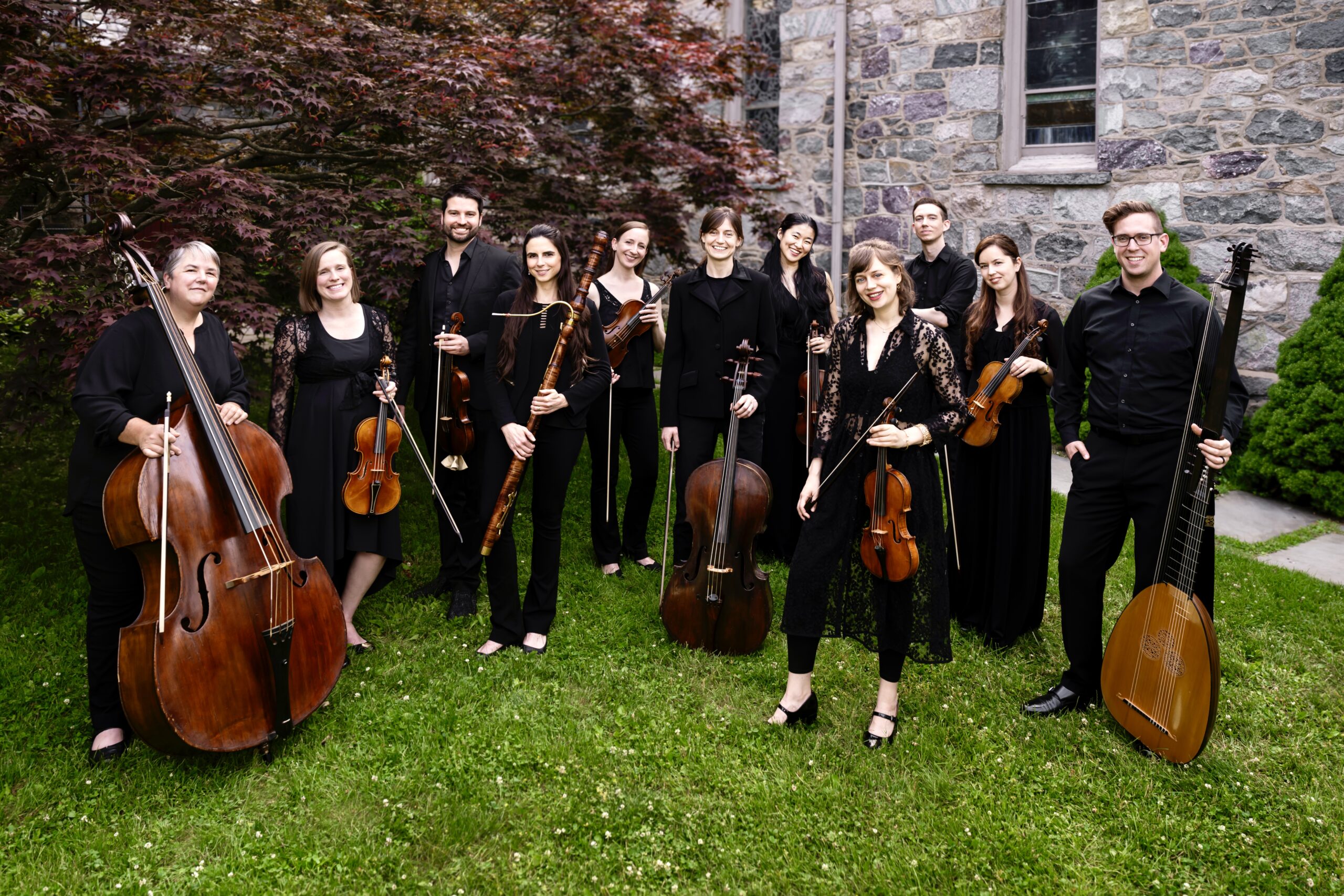 An ensemble of eleven musicians poses with string instruments.