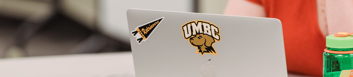 student using a laptop displaying UMBC branded stickers