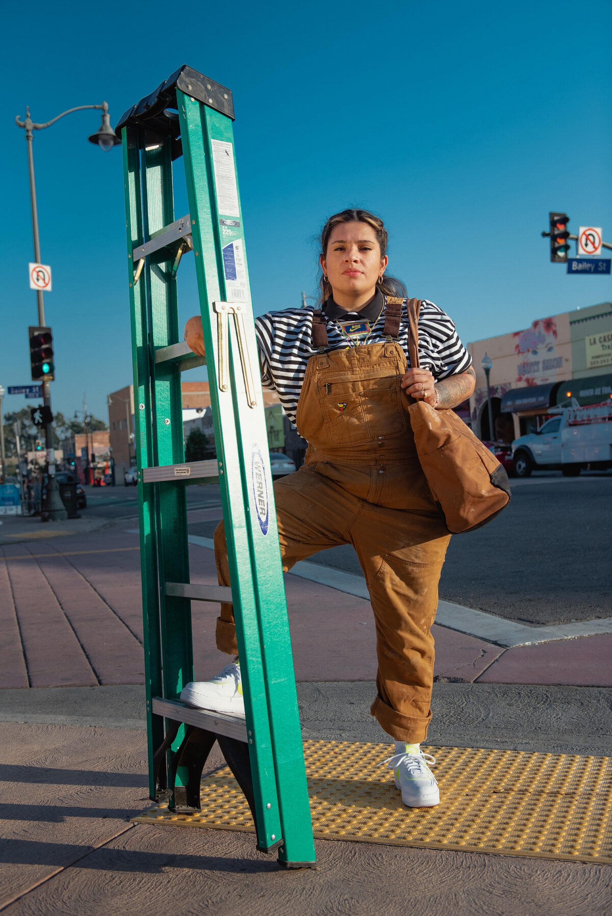 Artist Johanna Toruño stands next to a ladder. ©2020 theunapologeticstreetseries, all rights reserved.