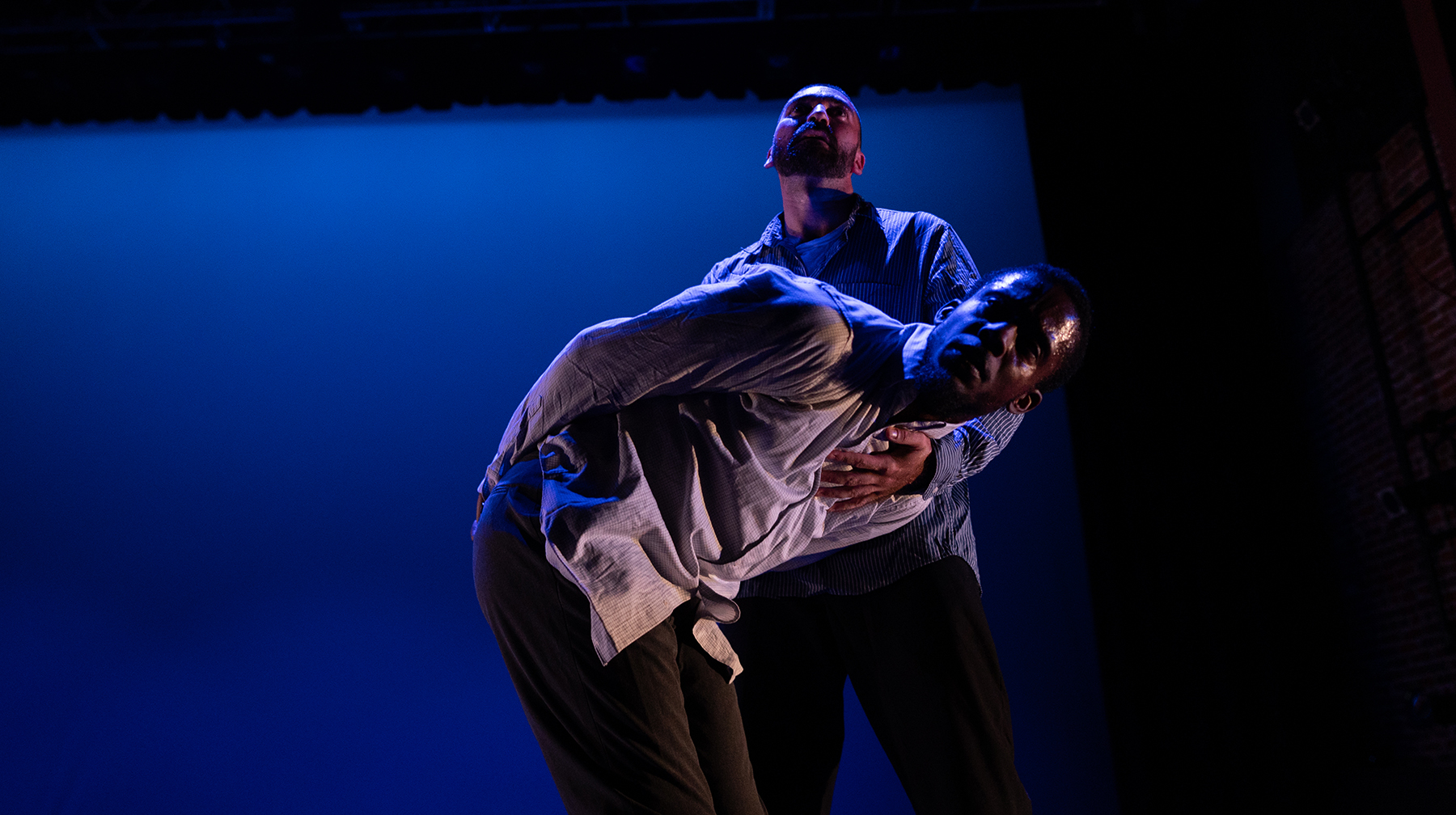 Against a deep blue background, two male dancers are locked in a pose.
