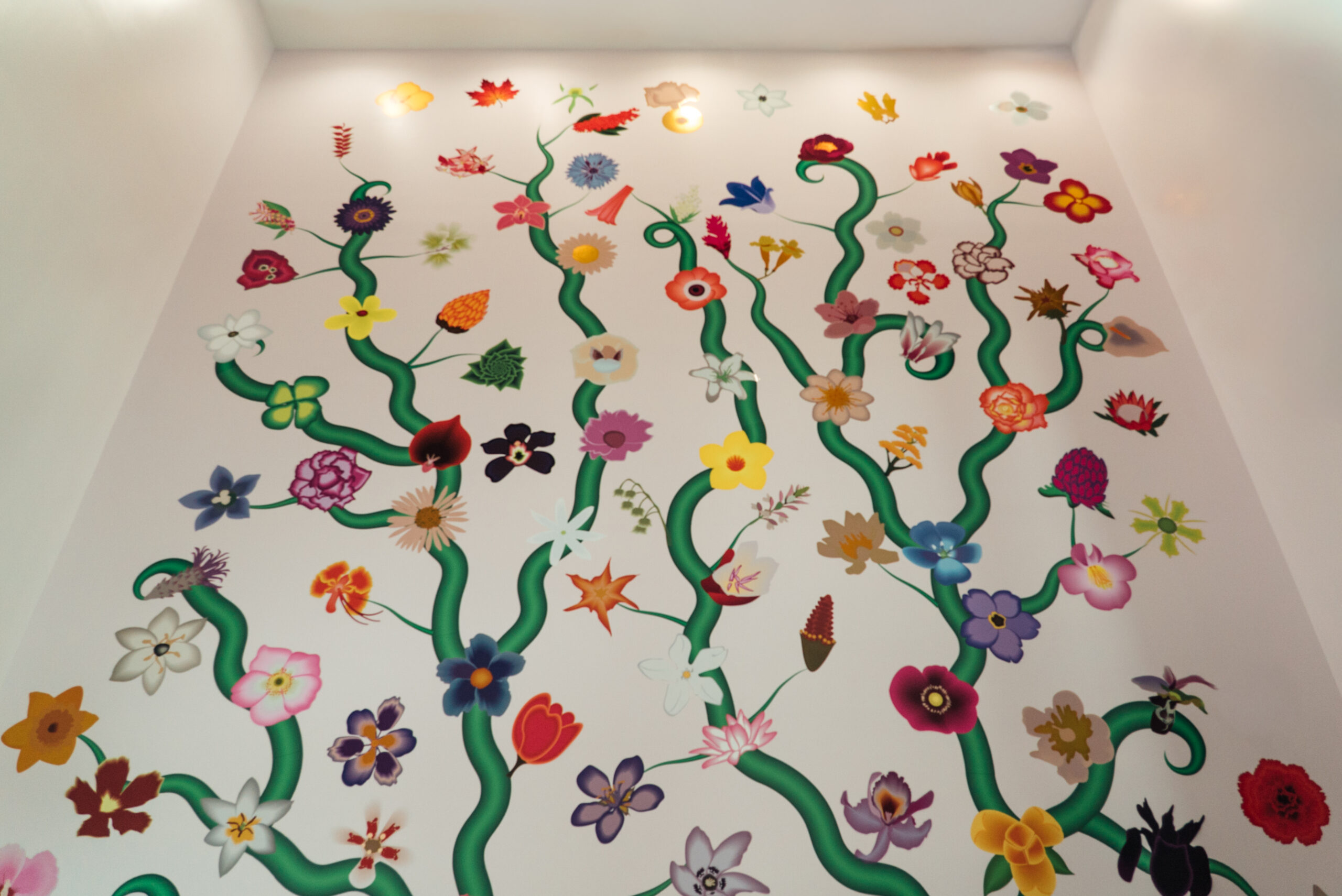 A wall with a design of brightly colored flowers branching off green tree limbs.