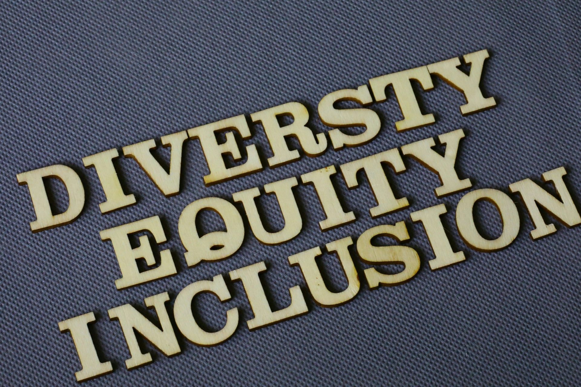 Wooden letters spelling "DIVERSITY," "EQUITY," and "INCLUSION" on a gray textured background. DEI