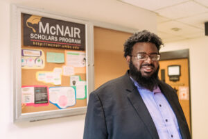 Michael Hunt stands next to bulletin board with sign reading "McNair Scholars Program"