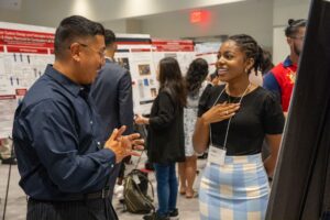 man speaks with young woman wearing a conference lanyard in a poster hall