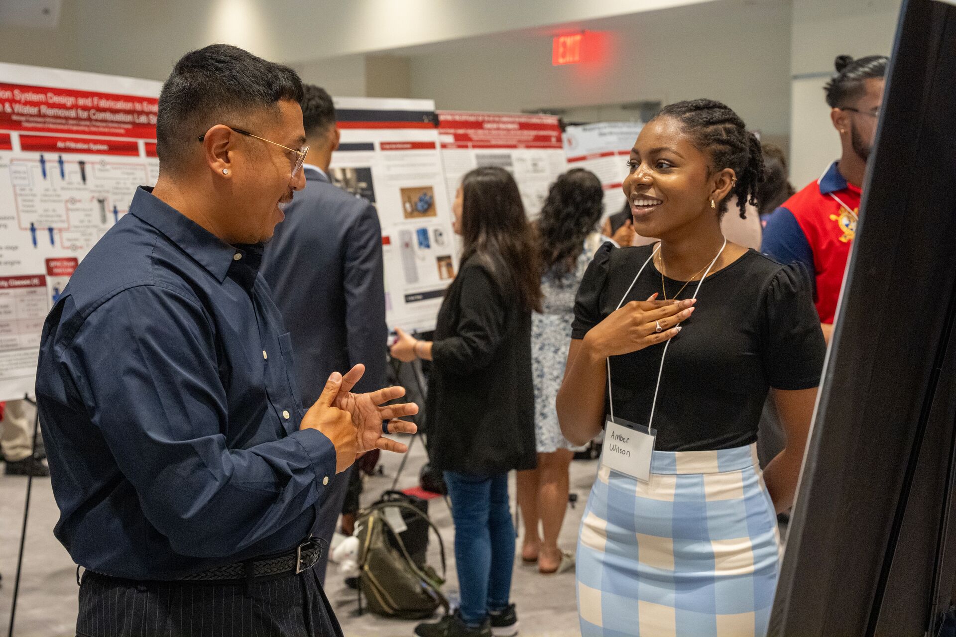 man speaks with young woman wearing a conference lanyard in a poster hall