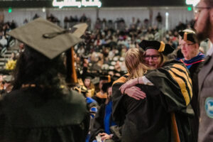 Jamie Gurganus, in formal academics robes hugs a student.