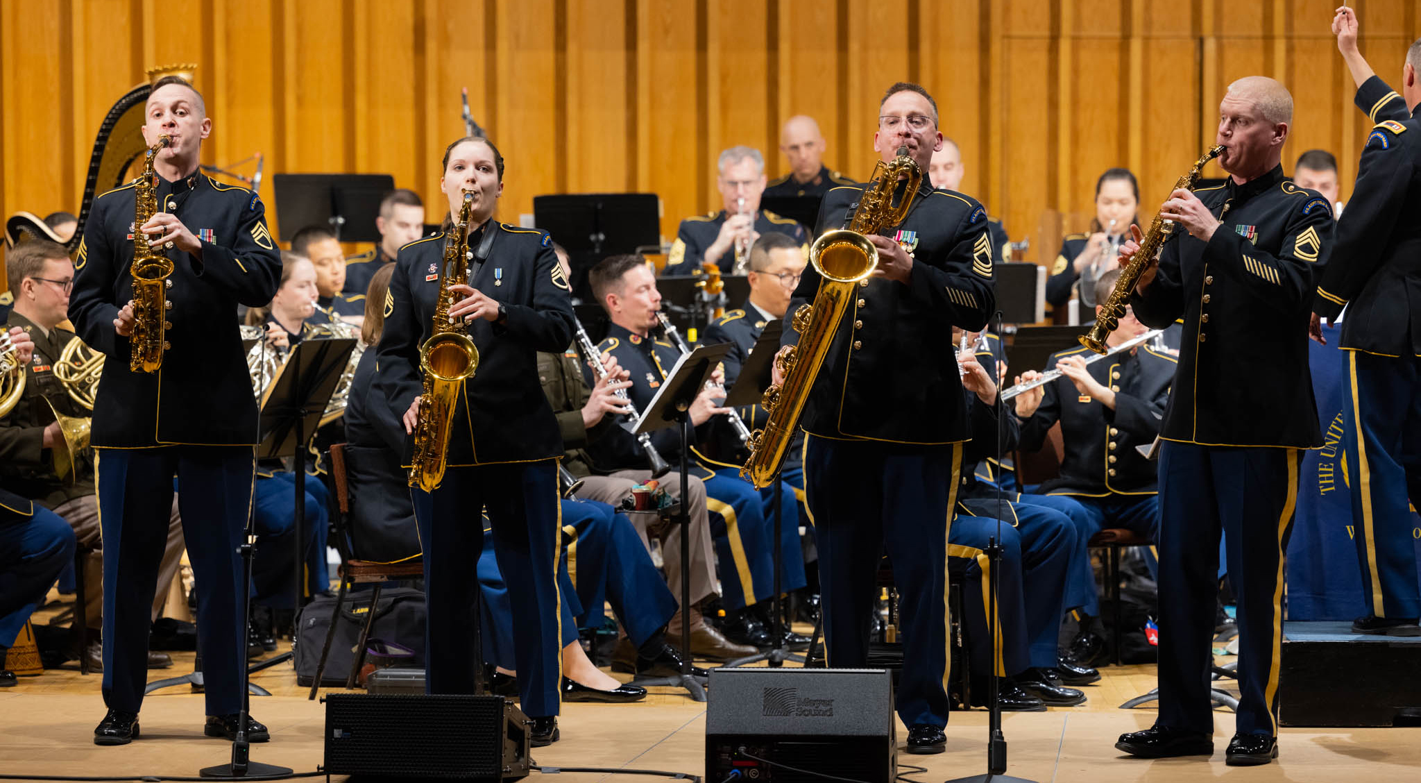 A group of saxophonists performs on stage in front of a larger group of musicians.