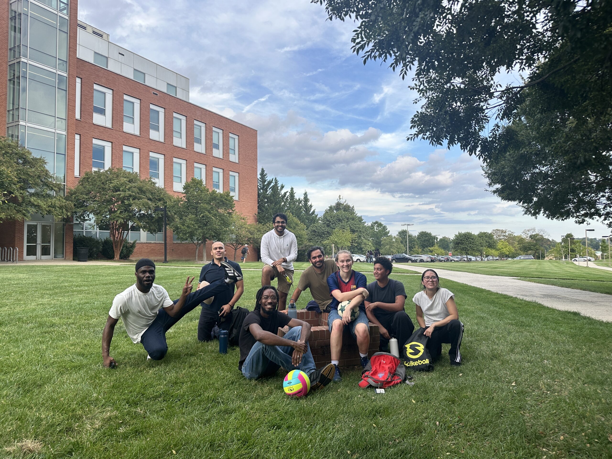 group photo of eight physics graduate students, including Maggie Williams, on the lawn outside the Physics Building