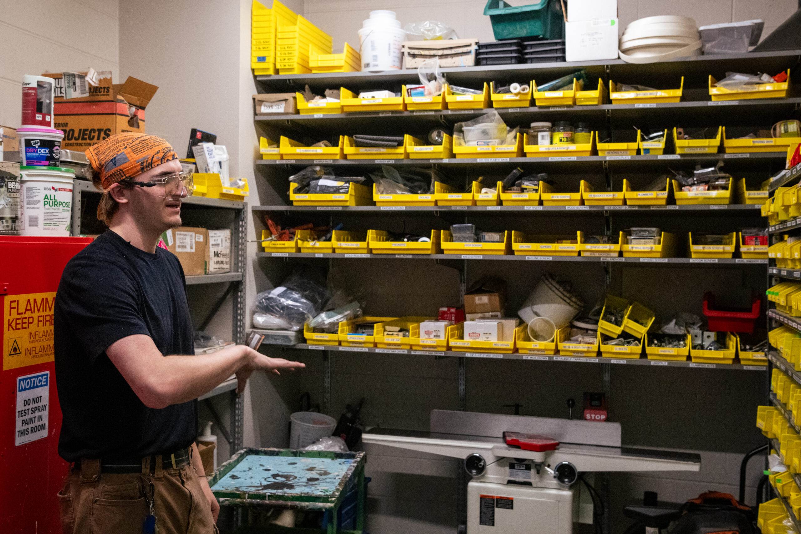 A student wearing an orange bandana and safety goggles explains the tools organized in yellow bins