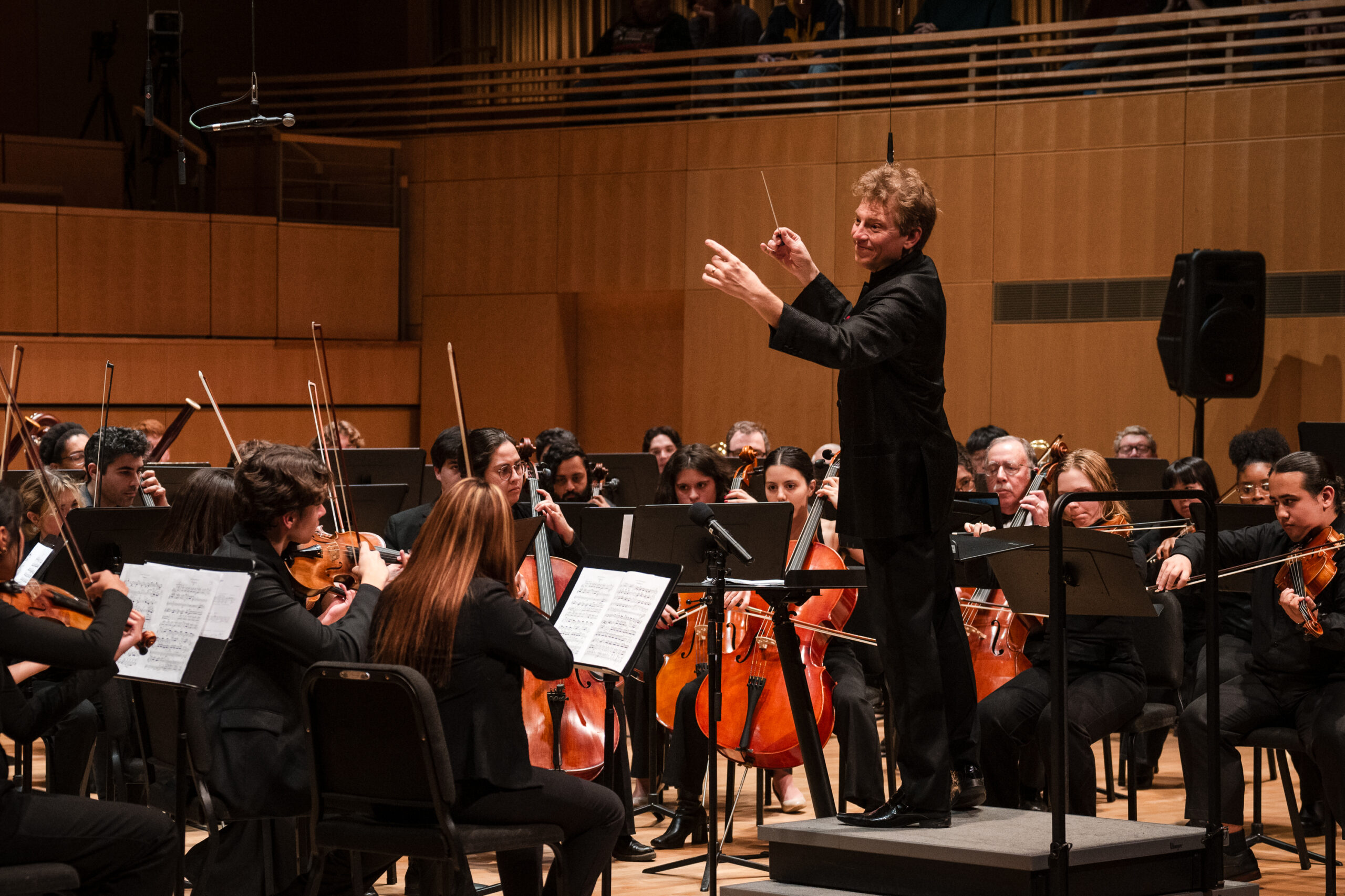 A conductor leads a symphony orchestra on a concert stage.