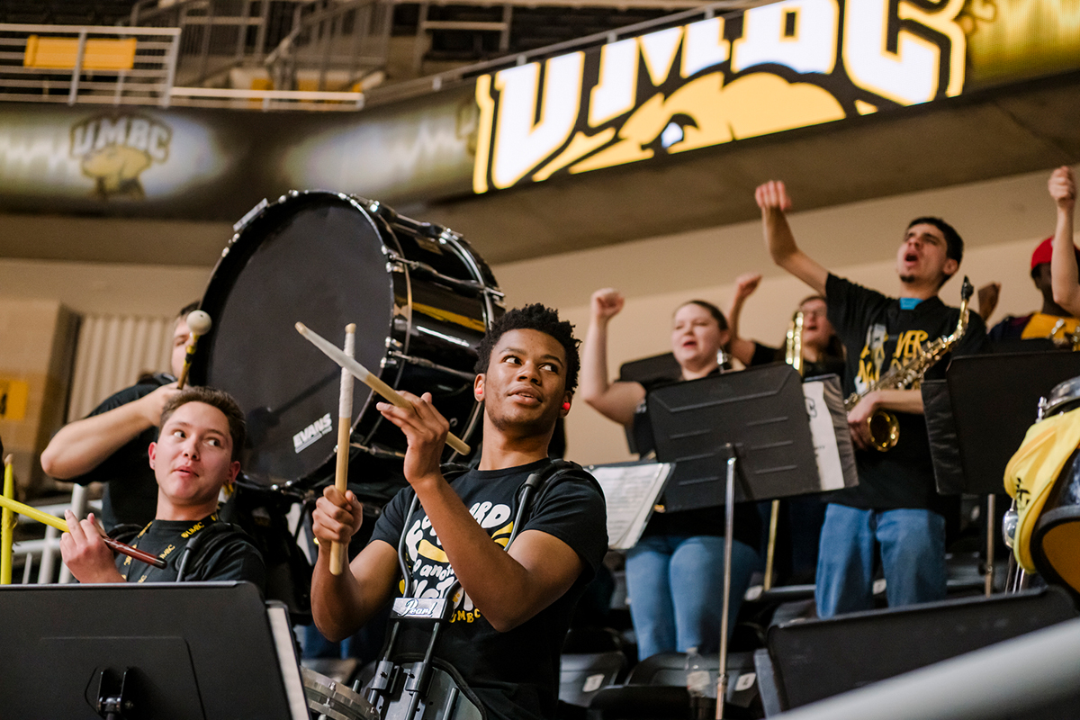 a student orchestra with drummers and brass instrument players wearing black and gold shirts