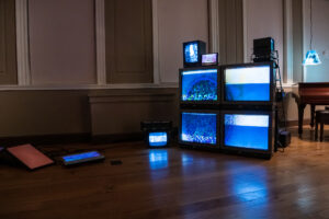 An art installation with stacked vintage televisions displaying blue static images in a dimly lit room.