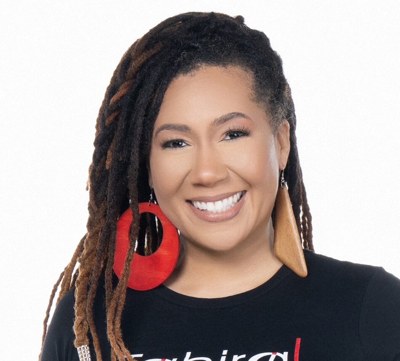 A woman with a medium skin tone and dark hair, wearing a large red earring and a black top, smiles at the camera.