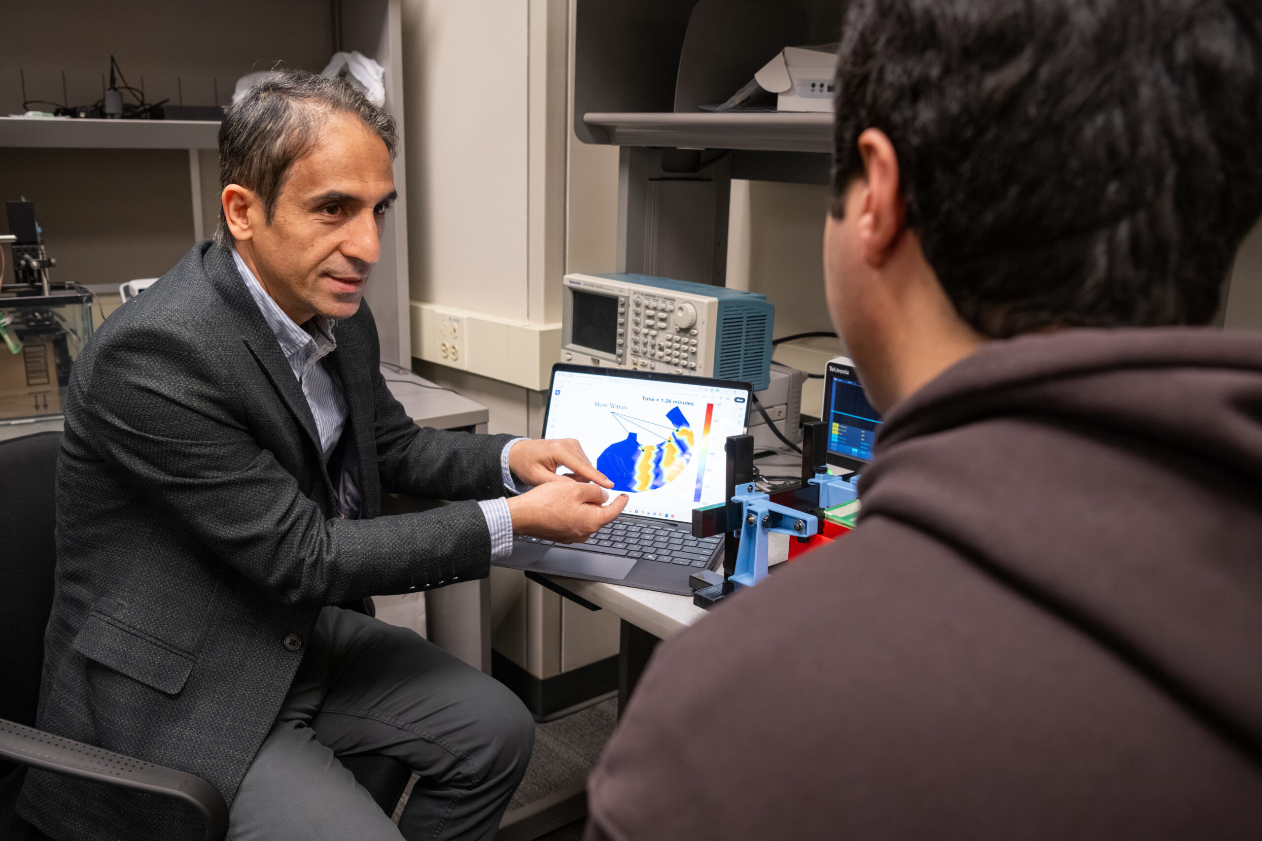 Kiani sits in front of a computer that shows a picture of a virtual stomach and talks with a student.