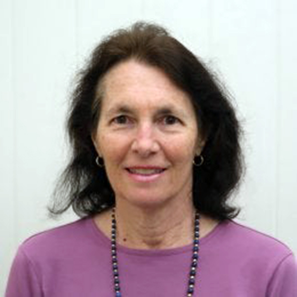 Against a white background, a white woman with dark hair and a lilac top smiles at the camera.