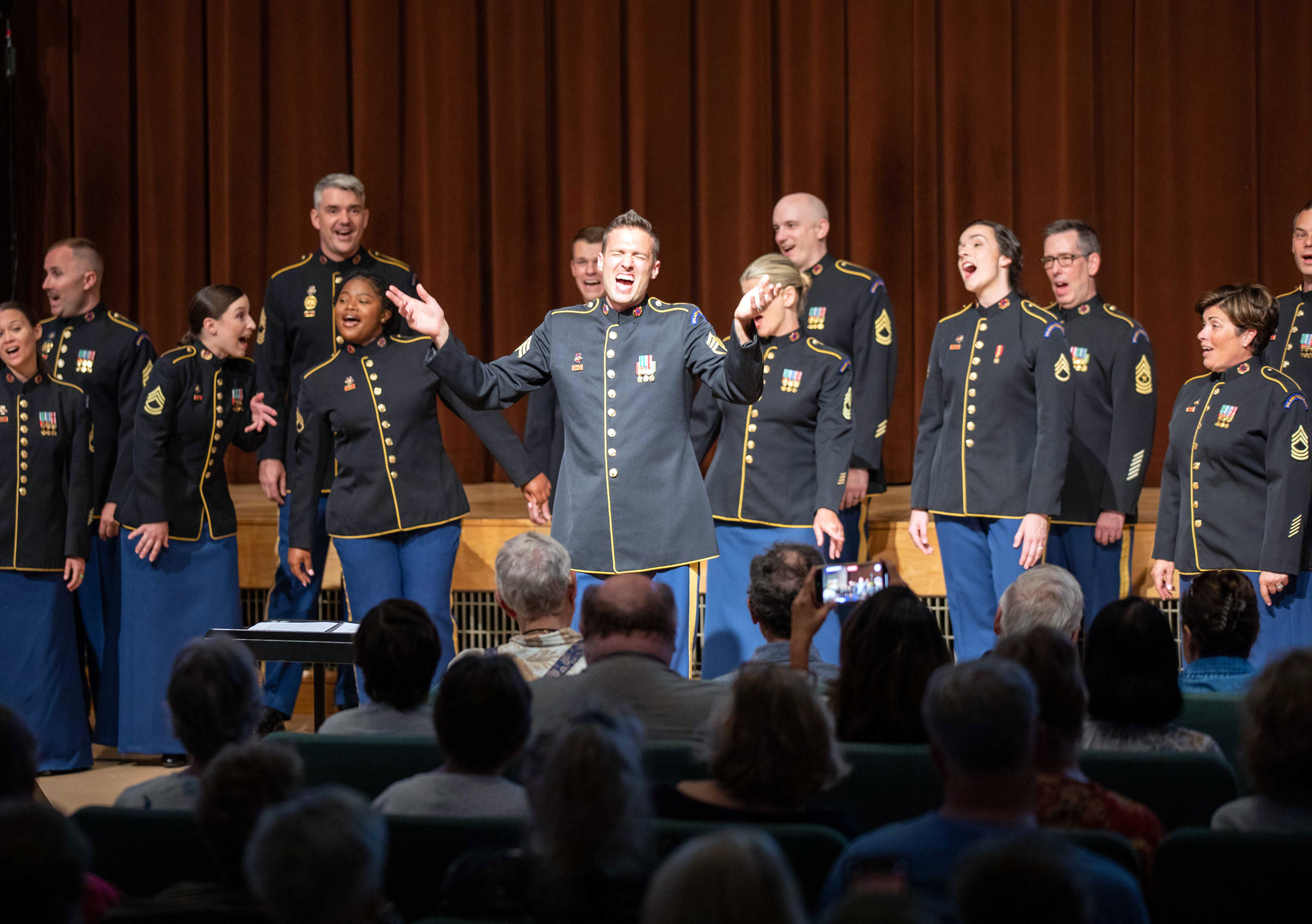 A group of singers in military uniforms perform before an audience.