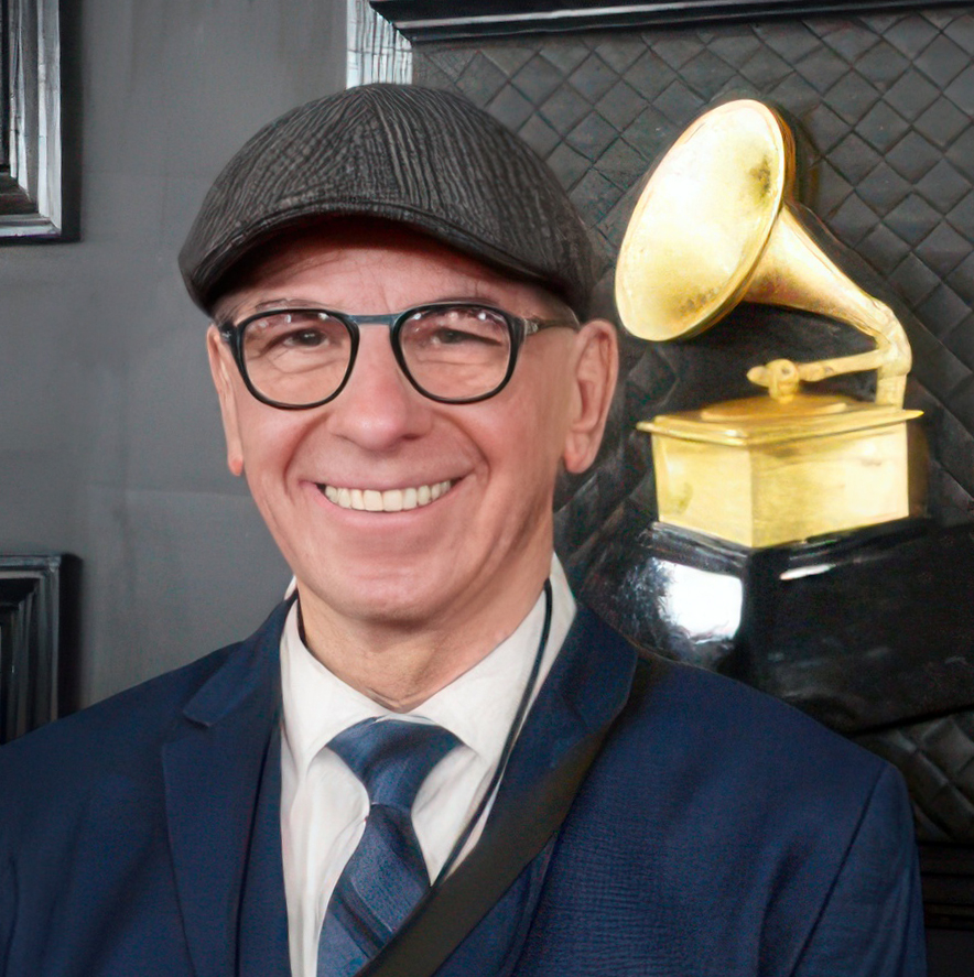 A white man wearing a cap and glasses poses next to an image of a gold colored Grammy Award, which resembles an old fashioned photograph.