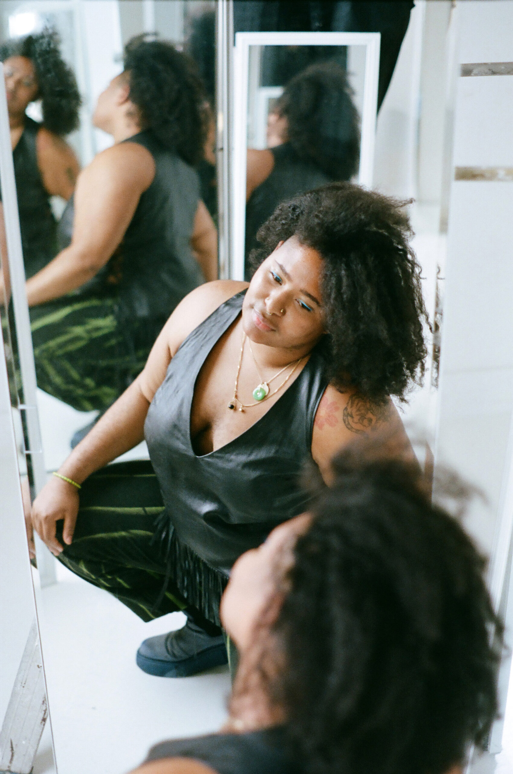 A Black woman in a dark outfit crouches toward the floor, and her image is reflected in multiple mirrors.
