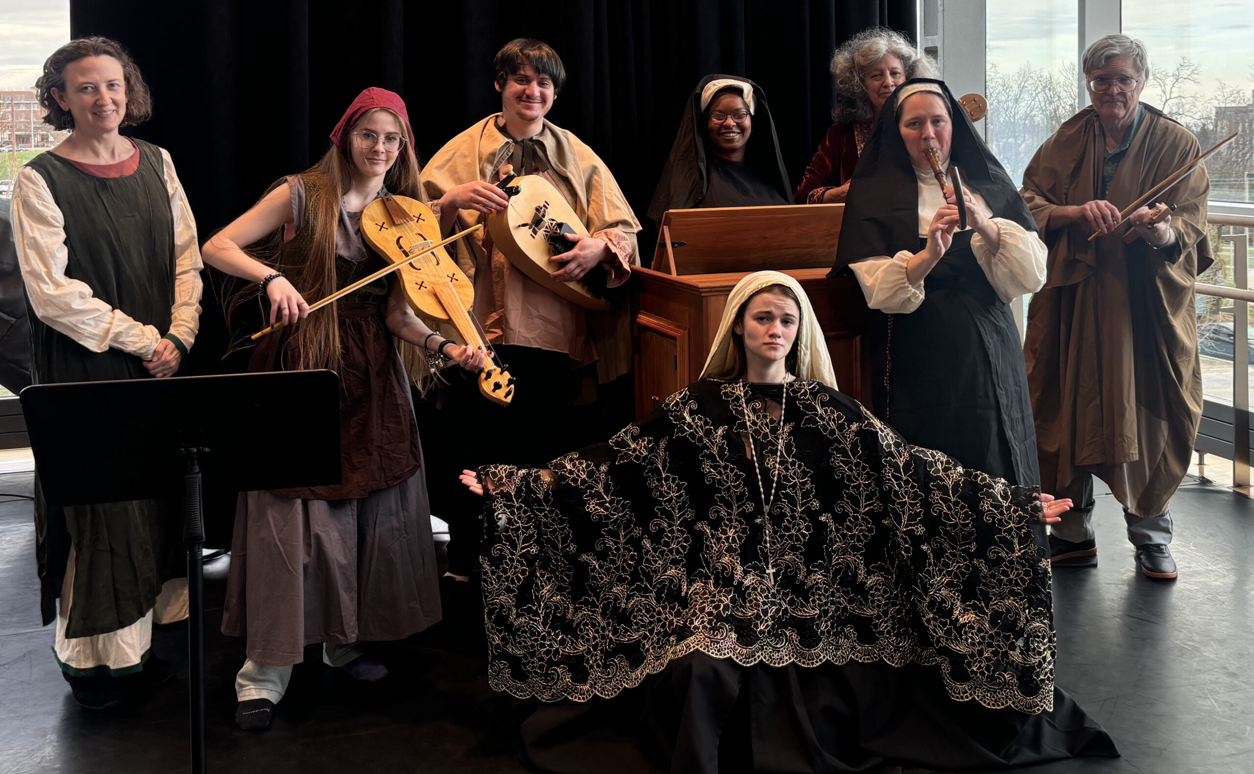 A group of people, some holding musical instruments, pose in medieval attire.