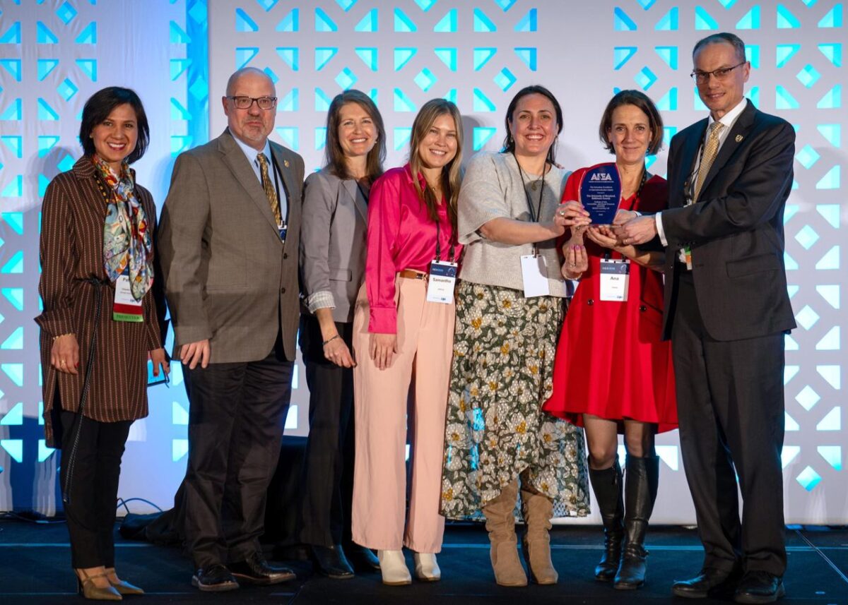A group of seven people in business attire gather together with two of them holding an award made of glass