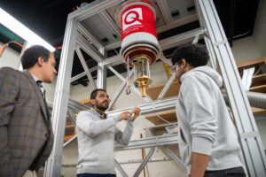 Daniel Suárez-Forero, Edgar Nicolás "Nico" Rueda-Becerra, and Yohannes Girma stand beneath a large, red, cylindrical instrument in the laboratory