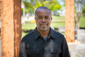 A man smiles for a headshot outdoors with blurred trees in the background
