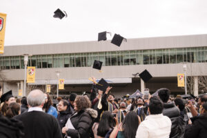 large crowd in commencement regalia, students throwing their caps in the air