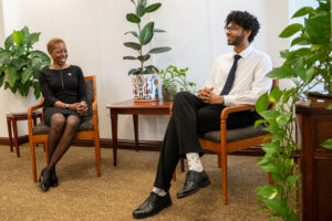 a woman in a business dress sits with a college senior, they're both smiling in conversation