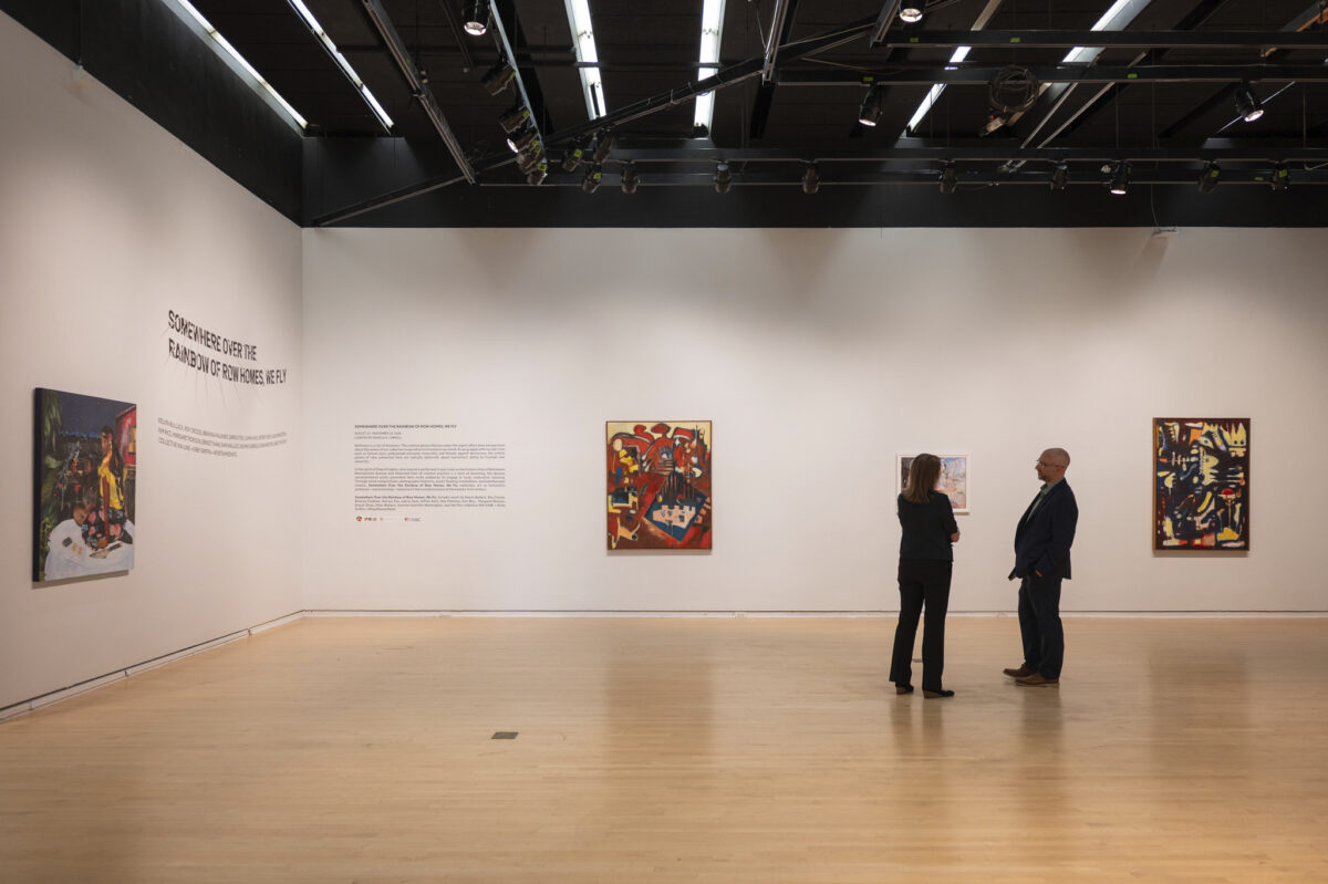 Two people stand in an art gallery looking at artworks hung on white walls.