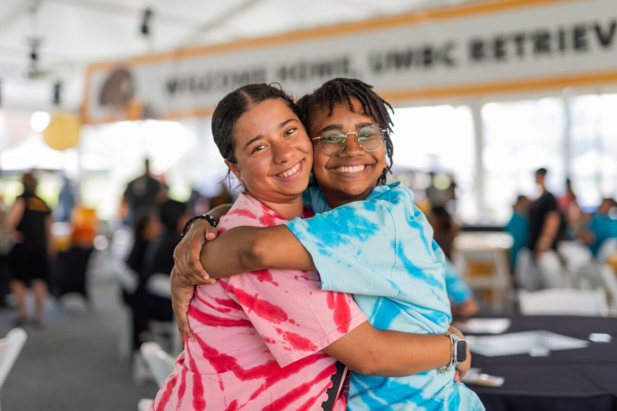 two welcome, retriever leaders in bright tie dyed shirts hug each other joyfully