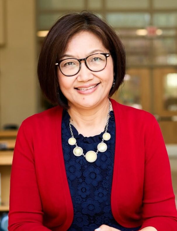 Headshot of a person with shoulder length dark hair and glasses, smiling.