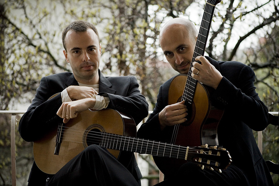 Two people sitting together, each holding a classical guitar.