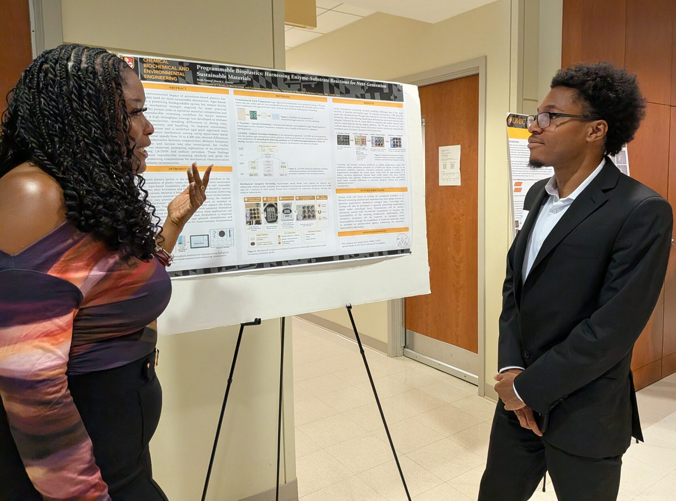 Two students stand near a summer research poster and talk.