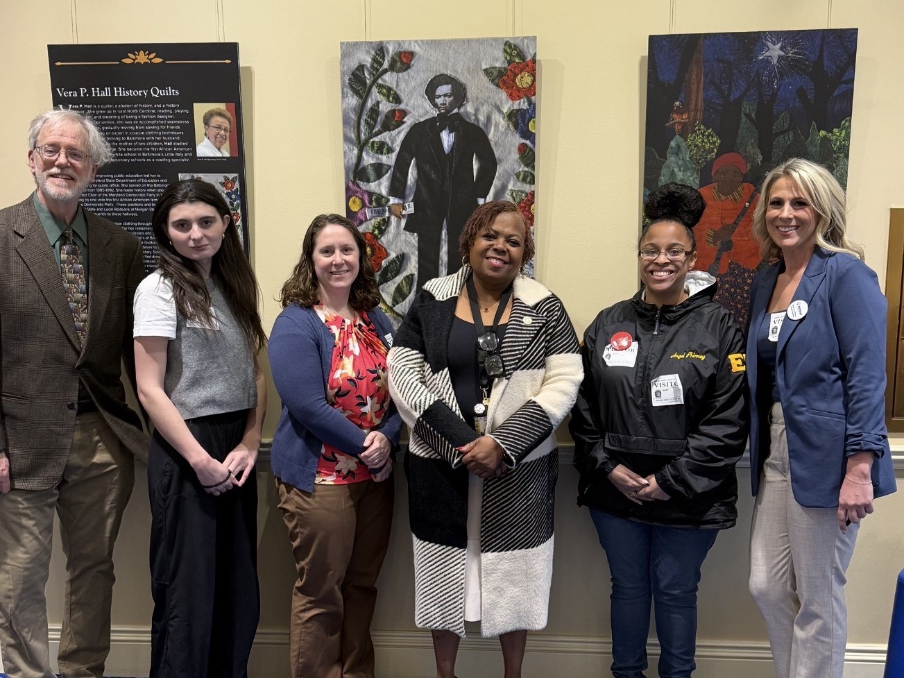 Kerri Evans, a professor of macro social work, stands with three students inside a lobby with a picture of Frederick Douglass in the background.